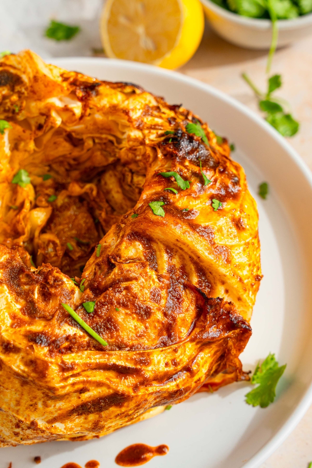 A white plate with a cabbage boil garnished with fresh parsley. The plate is on a tan counter with a small bowl of garnishes and lemon.