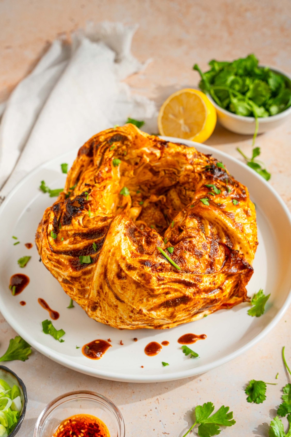 A white plate with a cabbage boil garnished with fresh parsley. The plate is on a tan counter with a small bowl of garnishes and lemon.