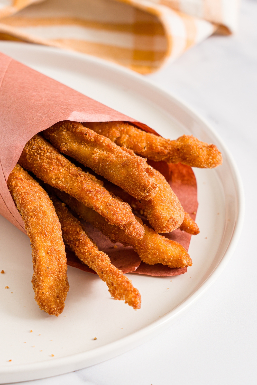 A white plate with fried homemade chicken fries wrapped in contact paper. The plate is on a marble counter with a yellow checkered napkin.