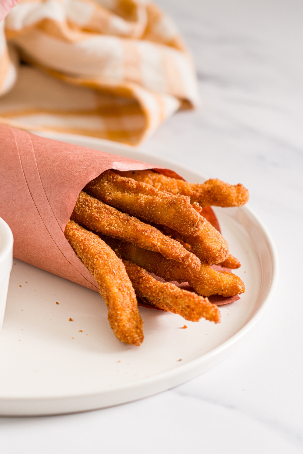 A white plate with fried homemade chicken fries wrapped in contact paper. The plate is on a marble counter with a yellow checkered napkin.