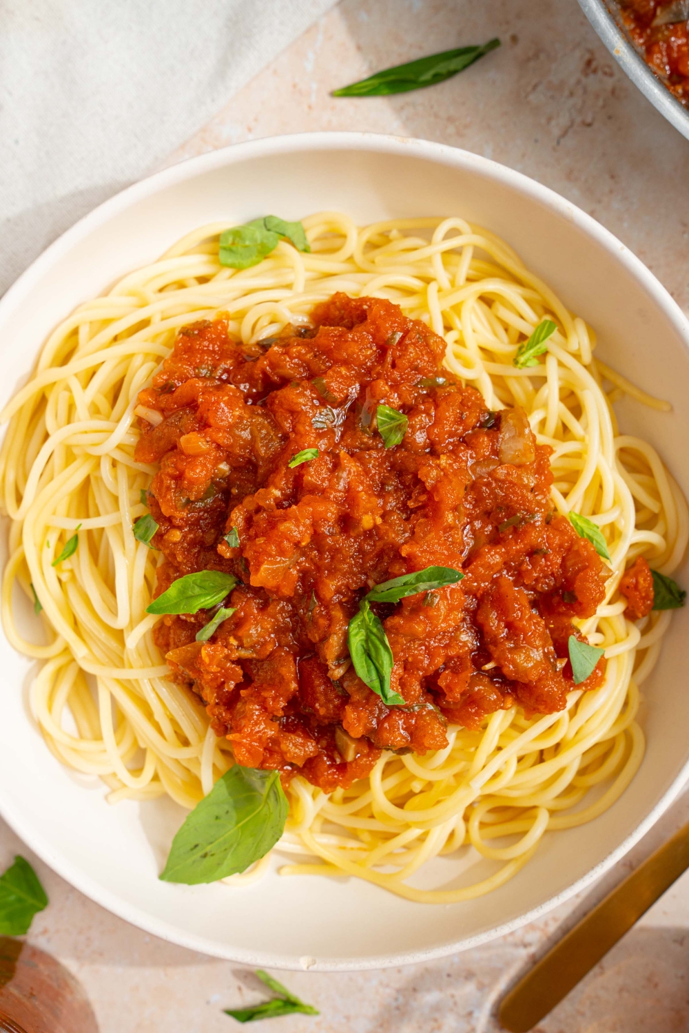 A bowl of spaghetti with homemade spaghetti sauce with fresh tomatoes. The bowl is garnished with fresh basil. The bowl is on a tan counter with a white cloth napkin.