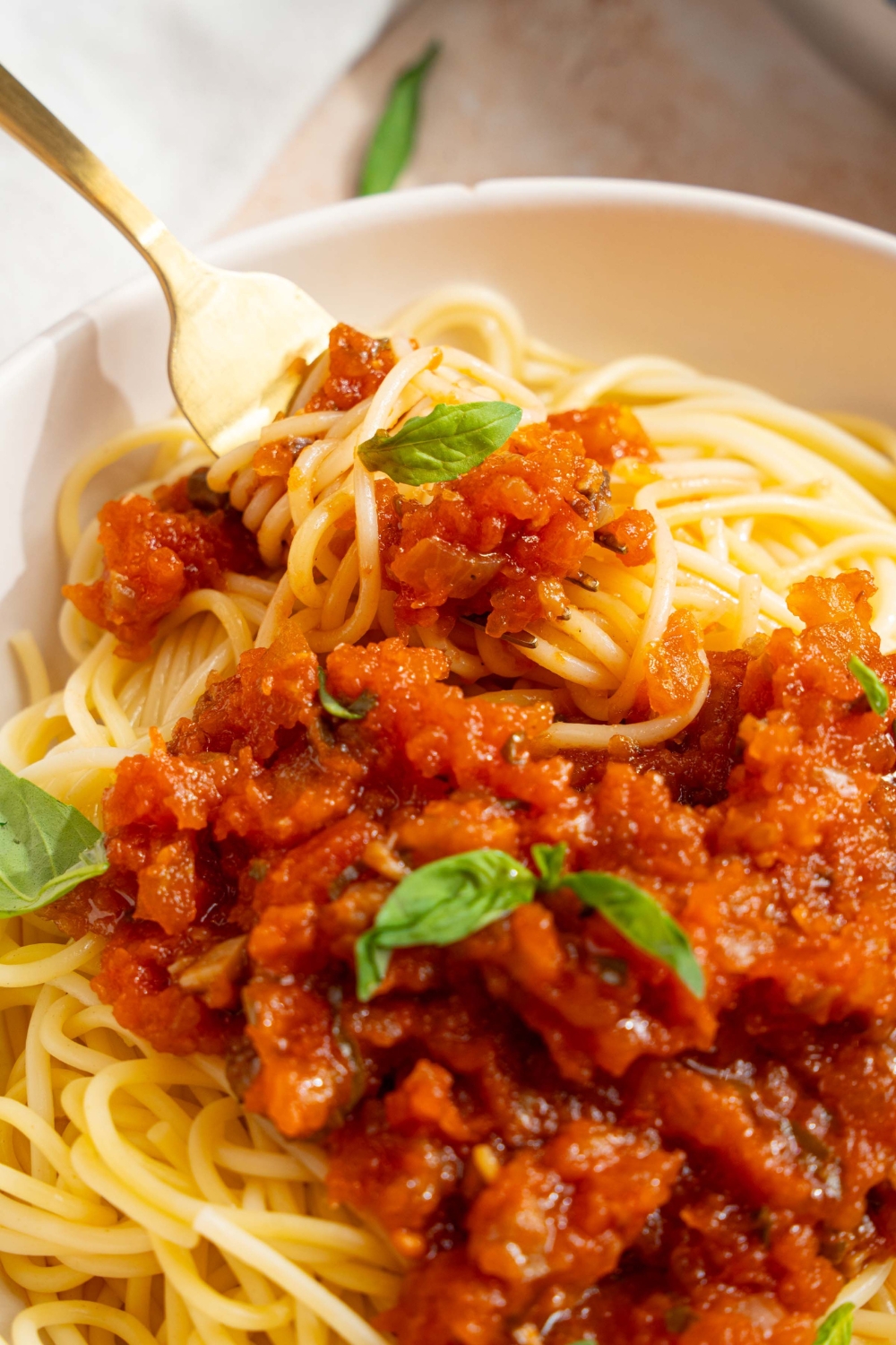 A bowl of spaghetti with homemade spaghetti sauce with fresh tomatoes. The bowl is garnished with fresh basil. There is a fork twirled in the pasta.