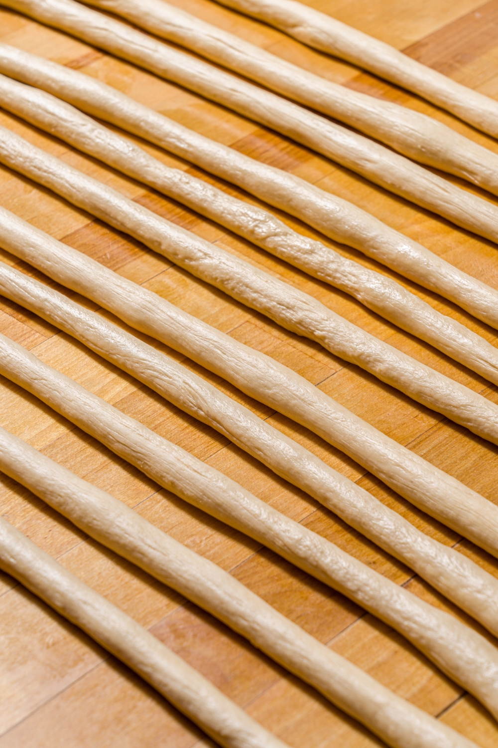 A wood counter with several strips of pretzel dough.