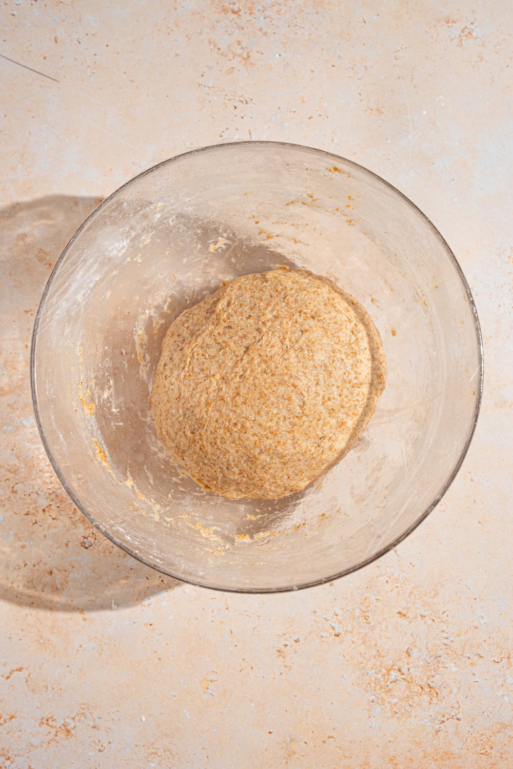 A glass bowl with Ezekiel bread dough. The bowl is on a tan counter.