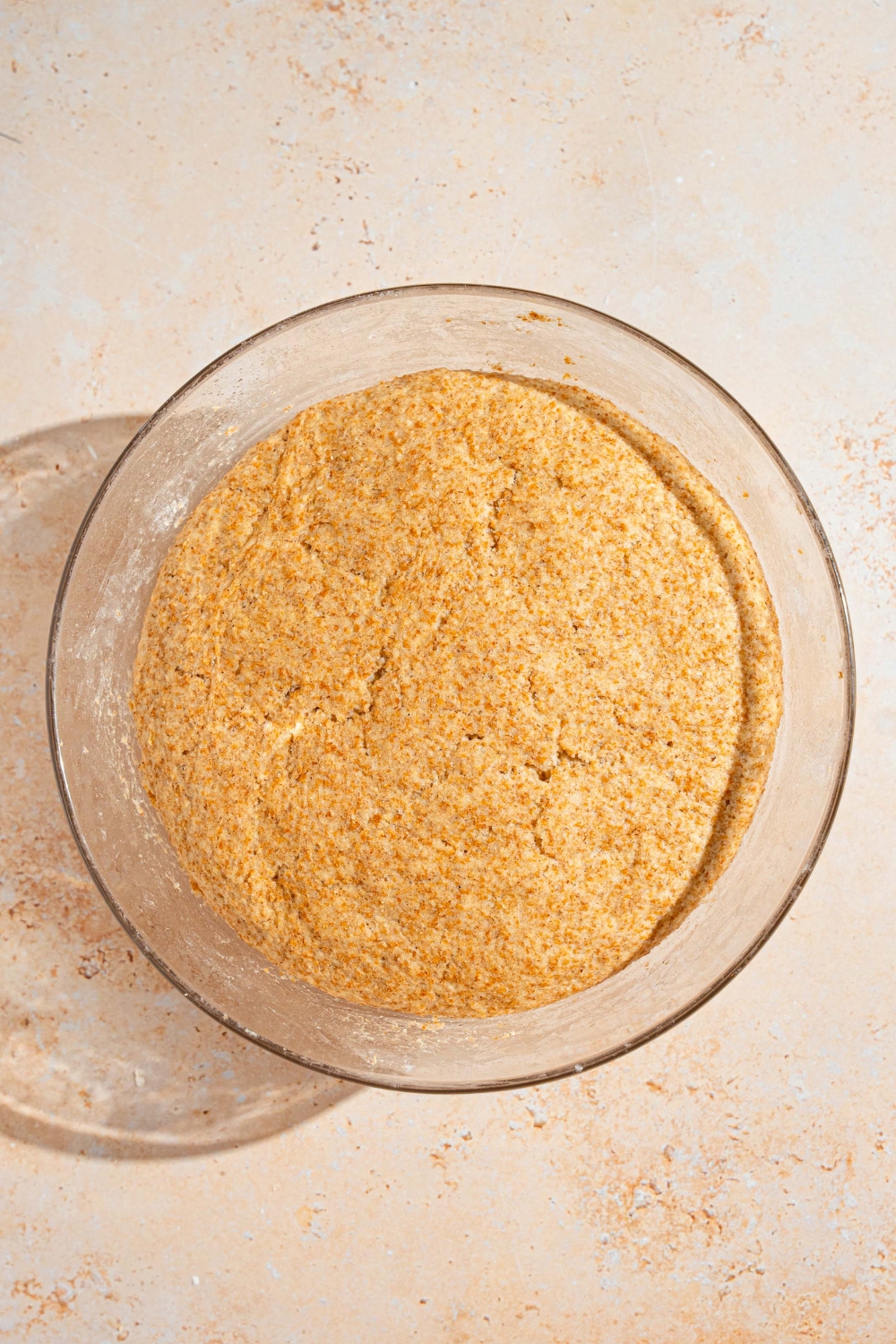 A glass bowl with risen Ezekiel bread dough. The bowl is on a tan counter.