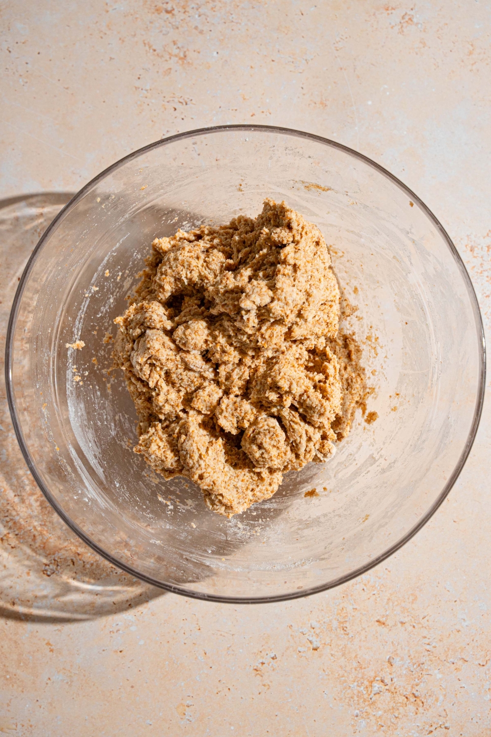A glass bowl with a Ezekiel bread dough mixture. The bowl is on a tan counter.