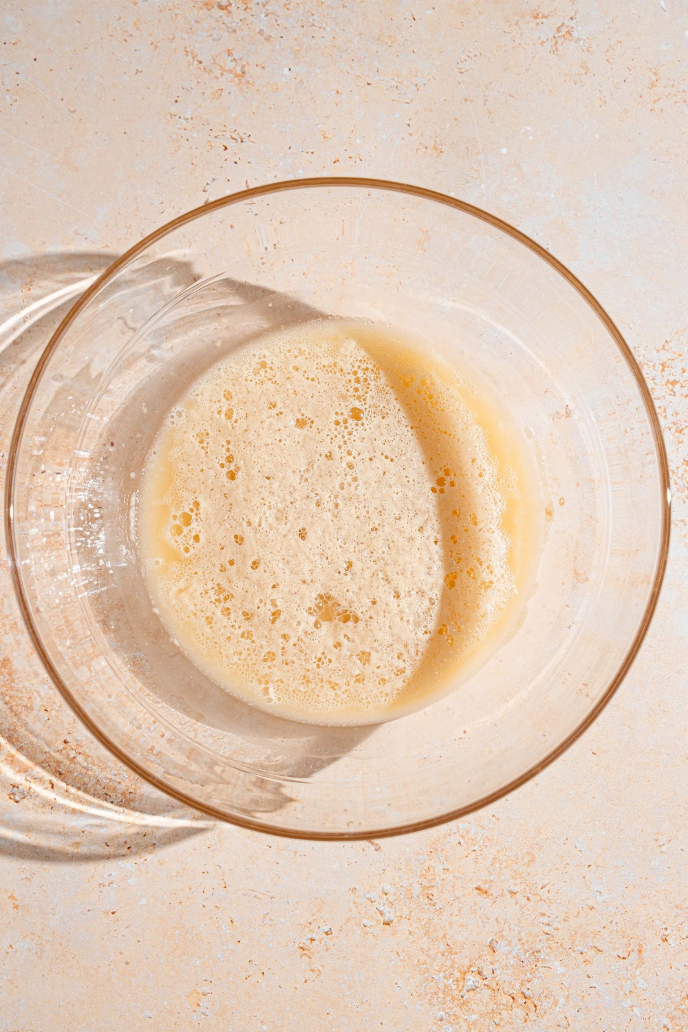 A glass bowl with a bloomed yeast mixture. The bowl is on a tan counter.