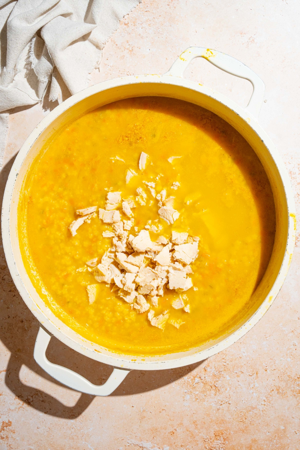 A stock pot of cooked Italian penicillin soup topped with diced chicken. The pot is on a white counter with a white cloth napkin.