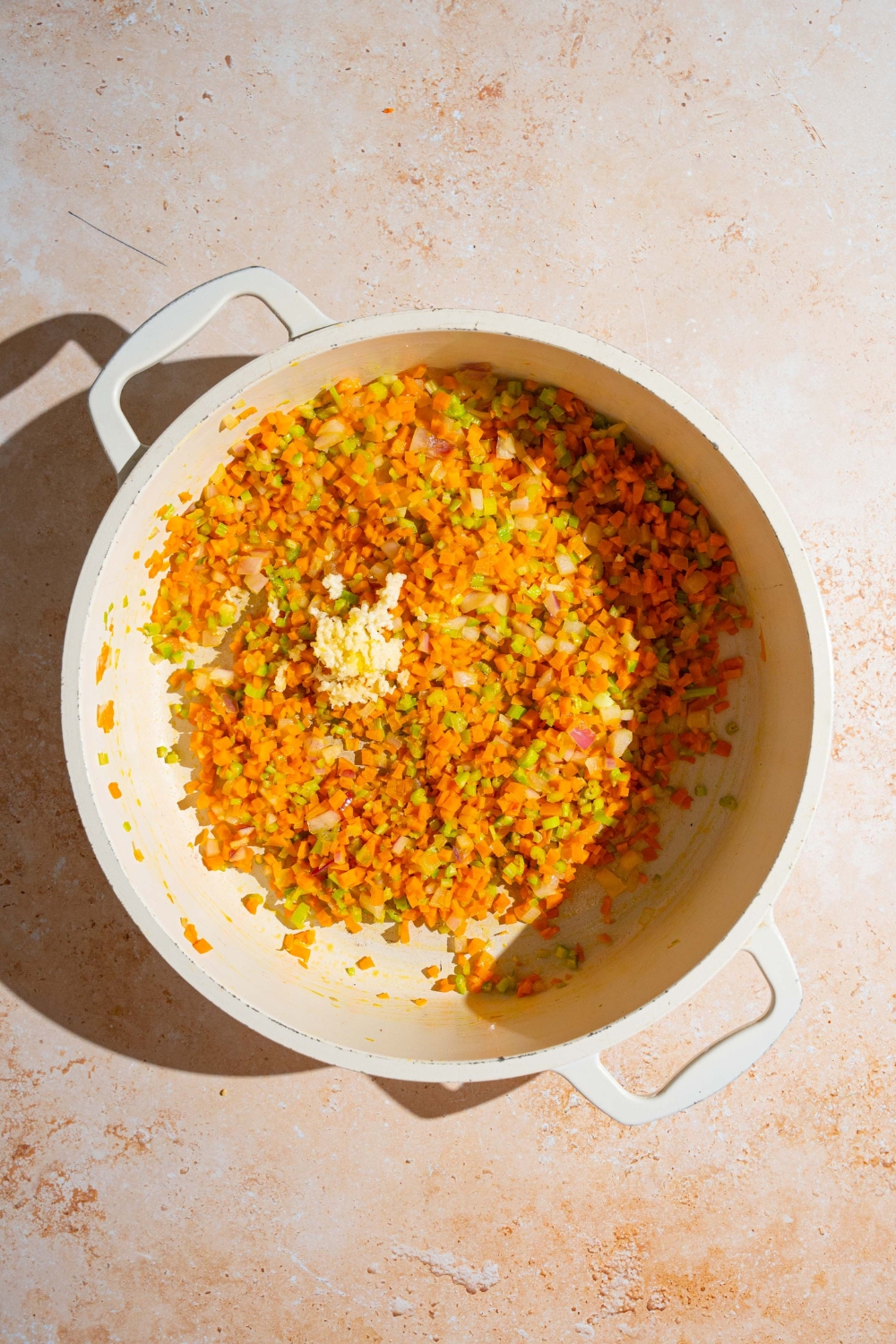 A stock pot with diced celery, onion, and carrots cooking in oil. The pot is on a tan counter.