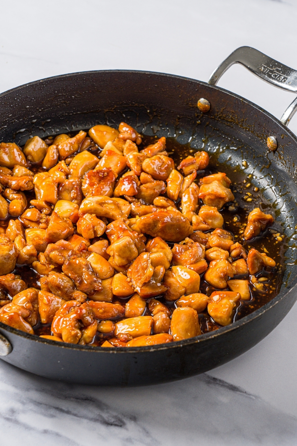 A skillet with cooked Korean sticky rice tossed in sauce. The skillet is on a marble counter.
