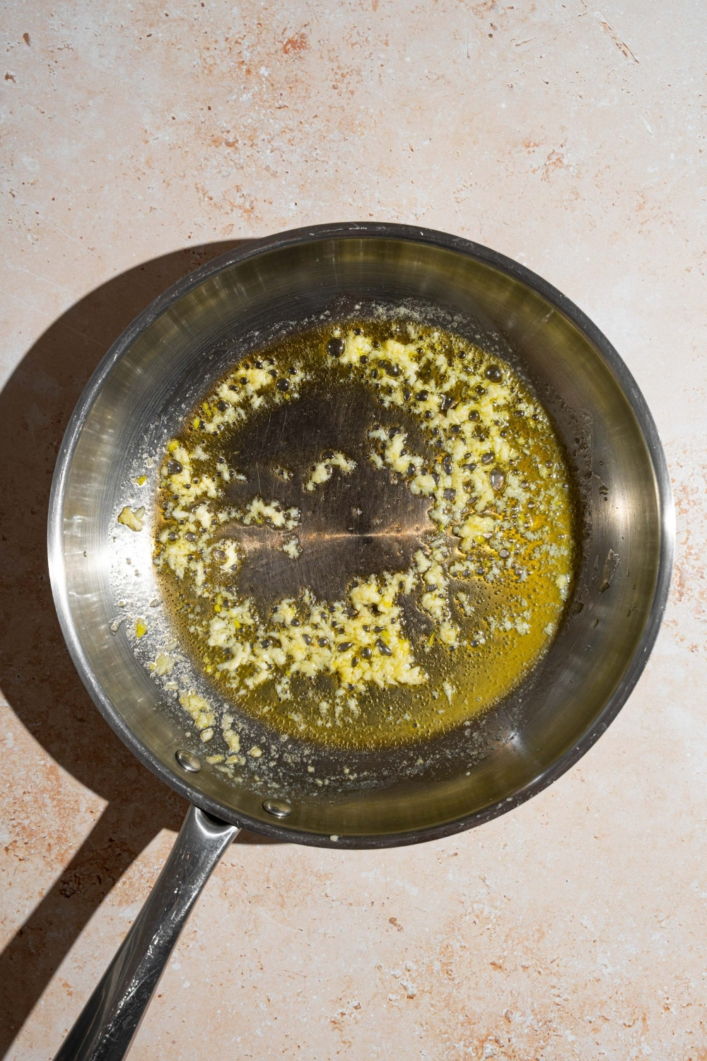 A skillet with garlic cooking in butter. The skillet is on a tan counter.