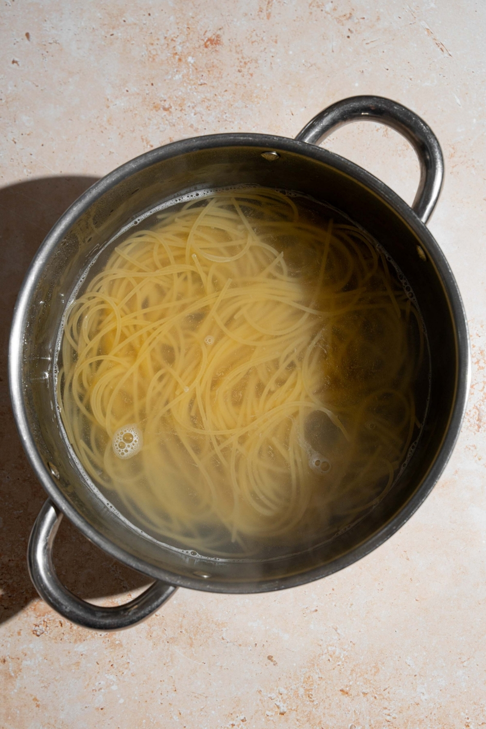 A stock pot with spaghetti cooking in water. The pot is on a tan counter.