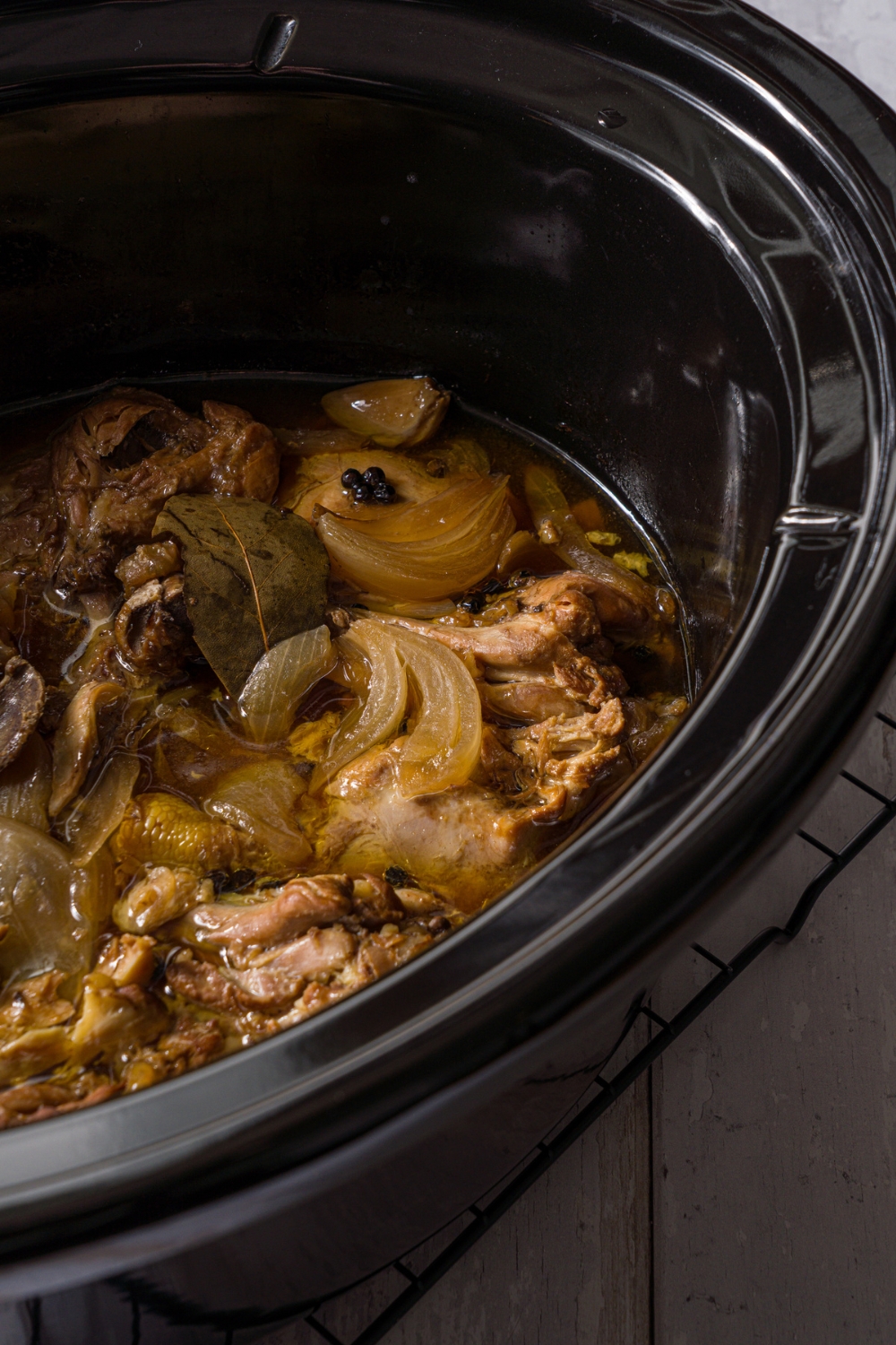 A slow cooker with slow cooked chicken adobo. The crockpot is on a wood counter.