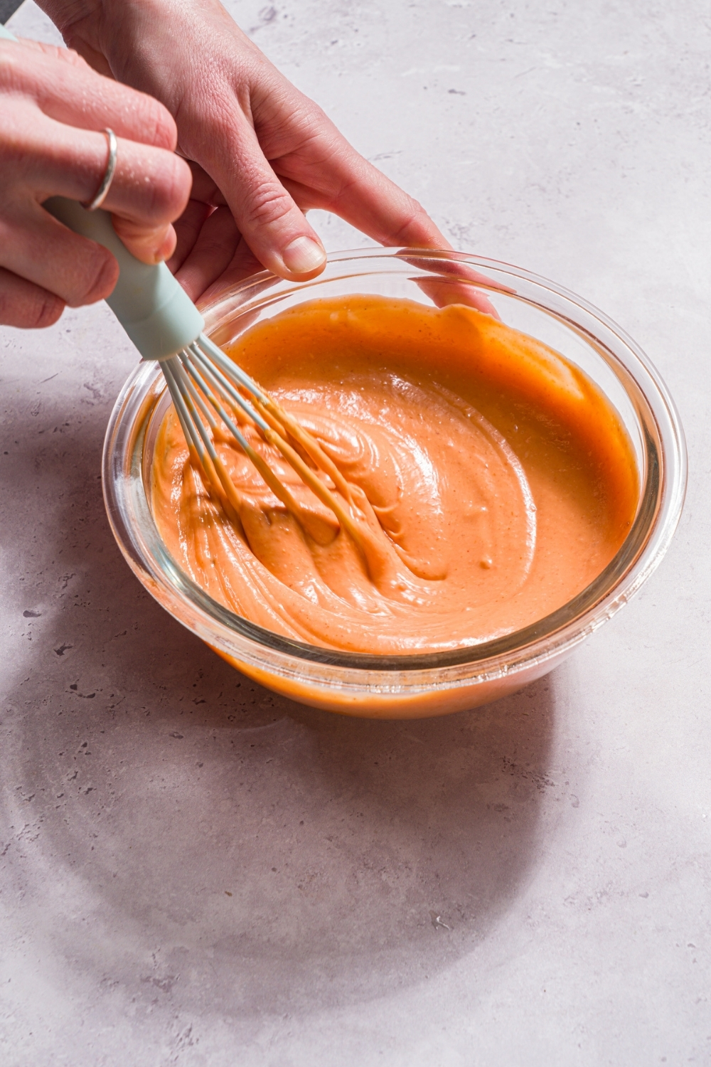 A glass bowl with a whisk mixing boom boom sauce. The bowl is on a stone counter.