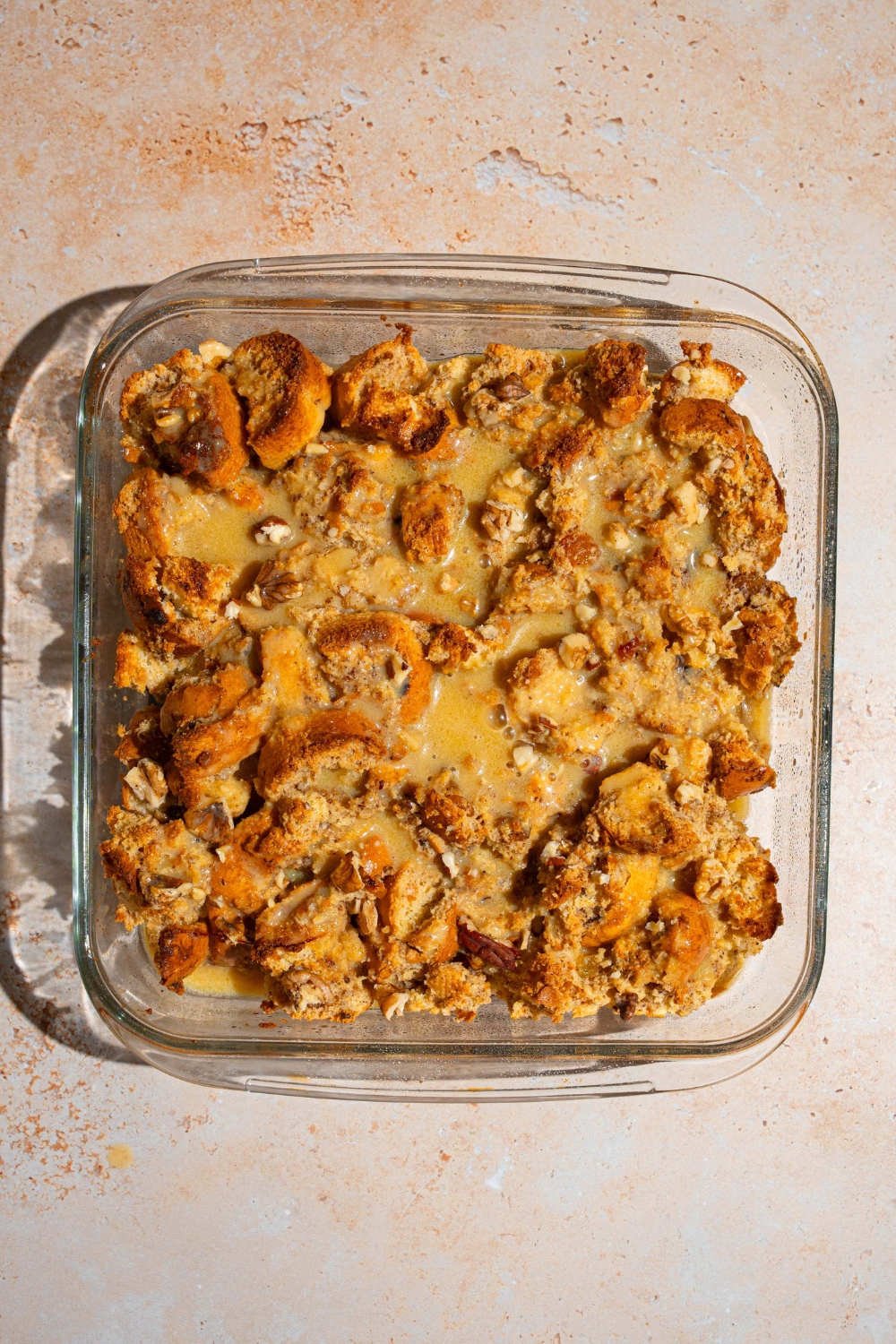 A baking dish with baked bread pudding topped with rum sauce. The dish on a tan counter.