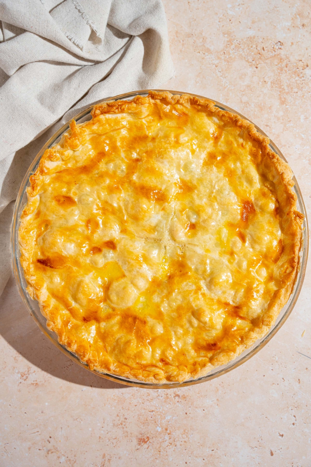 A whole baked chicken pot pie on a tan counter with a white cloth napkin.