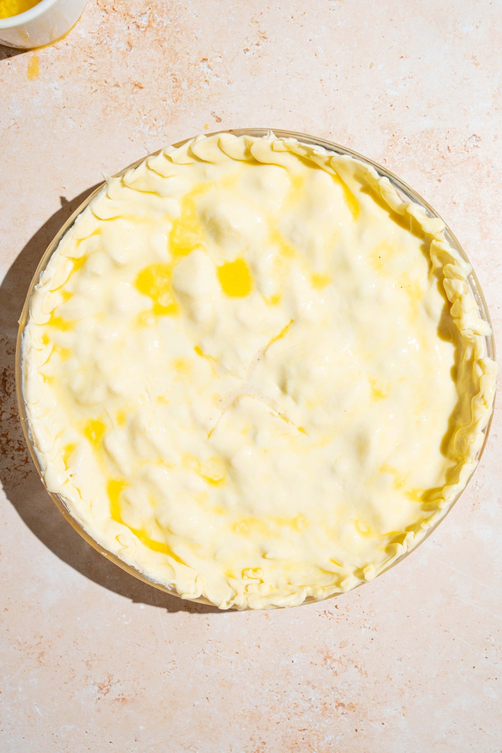 A whole unbaked chicken pot pie with the top crust covered in egg wash. The dish is on a tan counter.