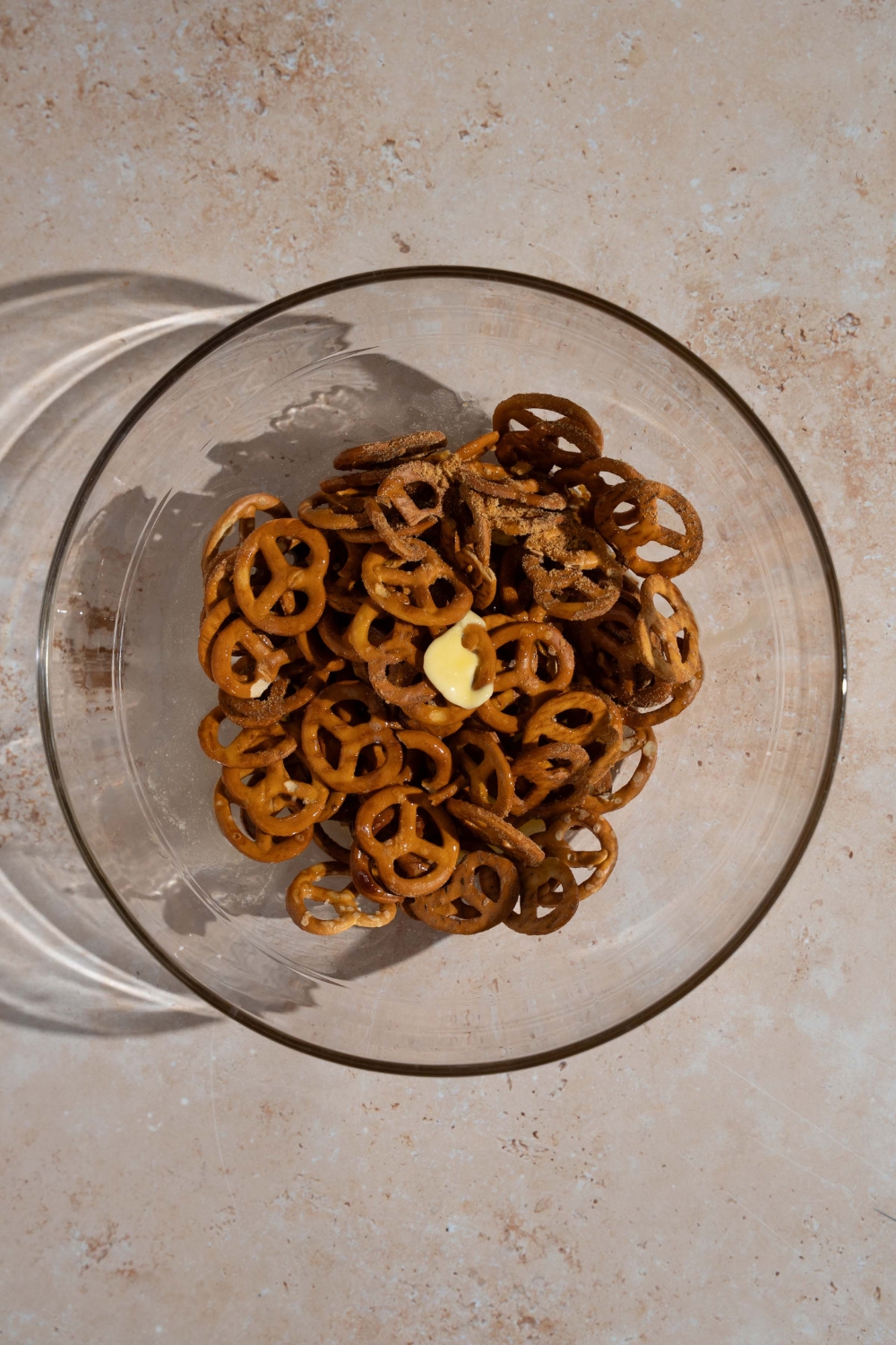 A glass bowl with pretzels topped with butter. The bowl is on a tan counter.