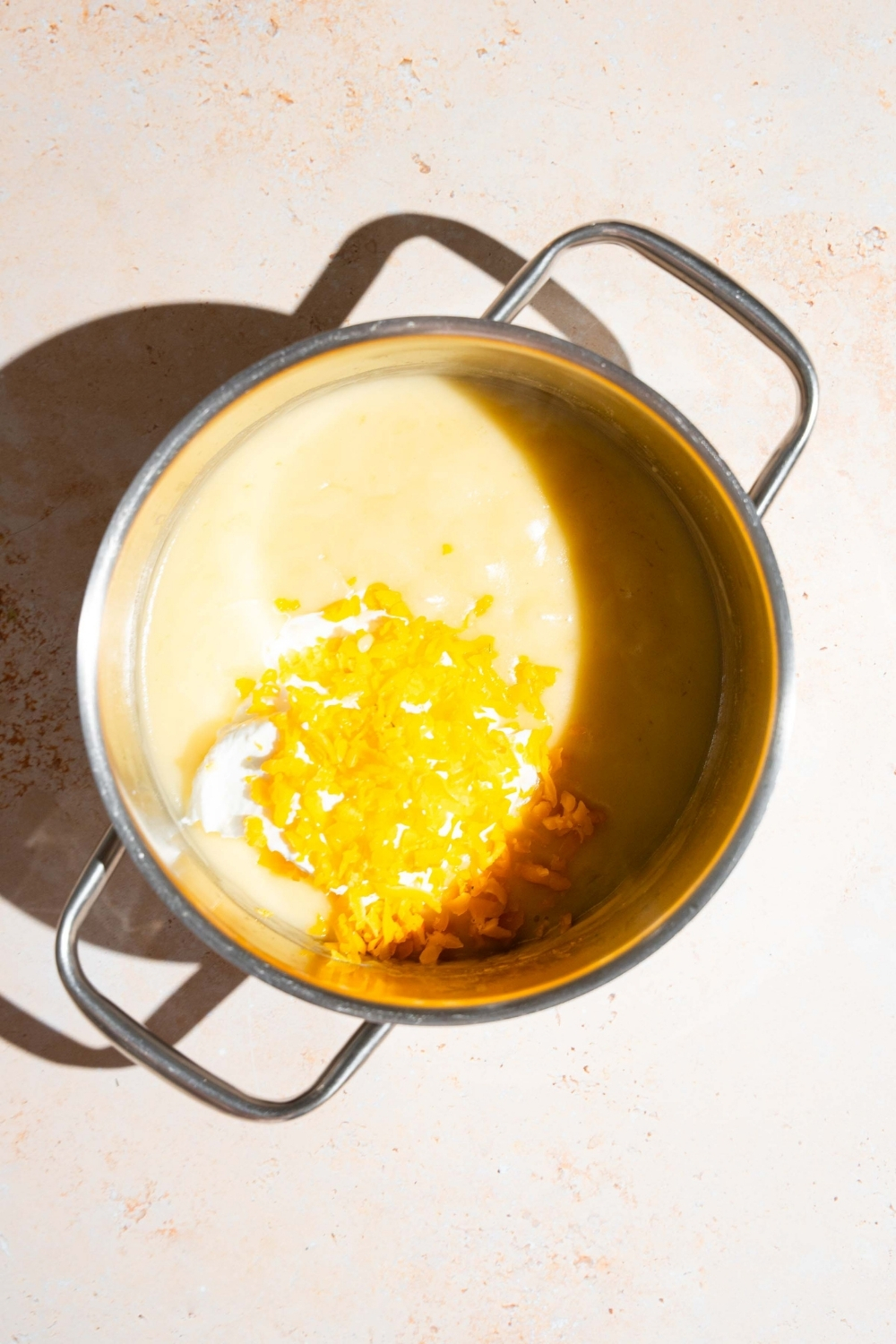A stock pot with sour cream sauce base topped with shredded cheddar cheese