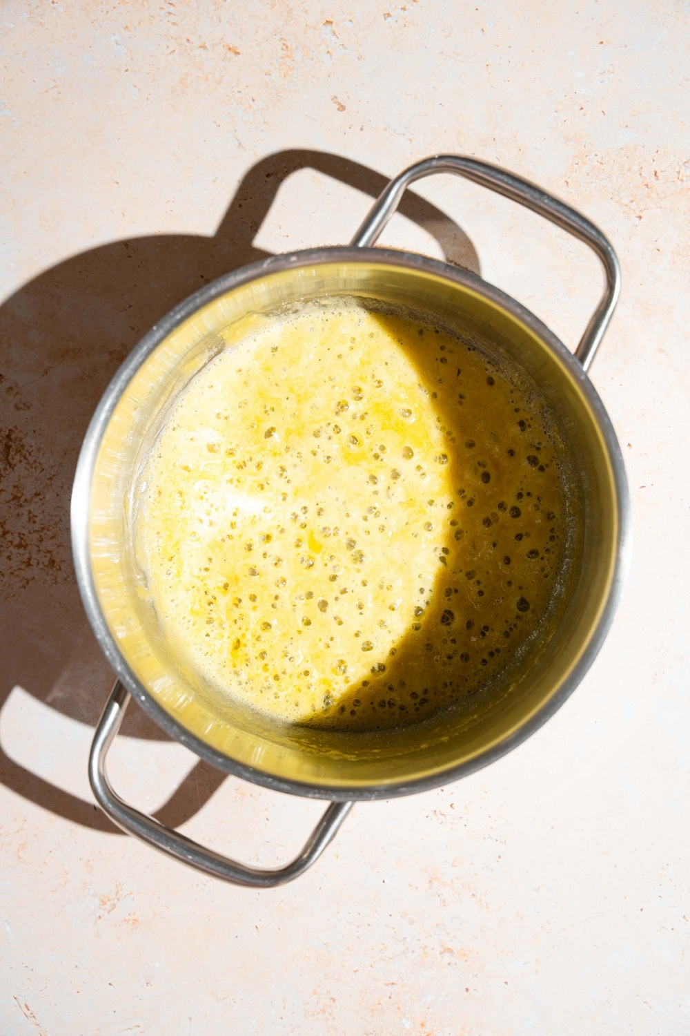 A stock pot with a roux cooking with butter. The pot is on a tan counter.