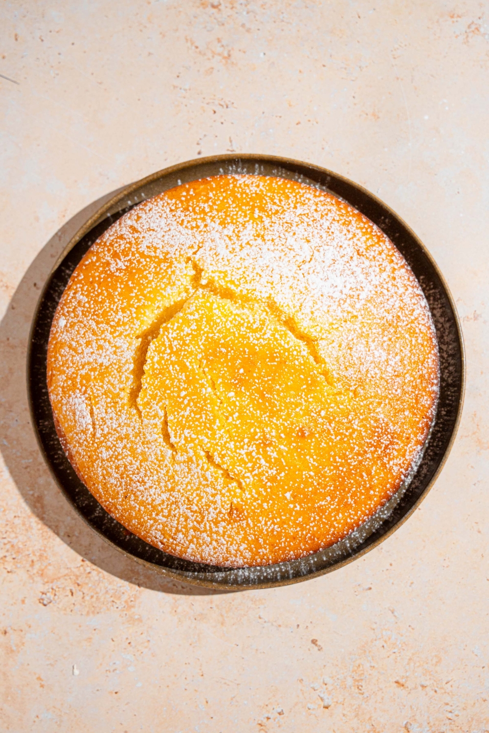 A cake pan with a baked French butter cake dusted with powdered sugar. The pan is on a tan counter.