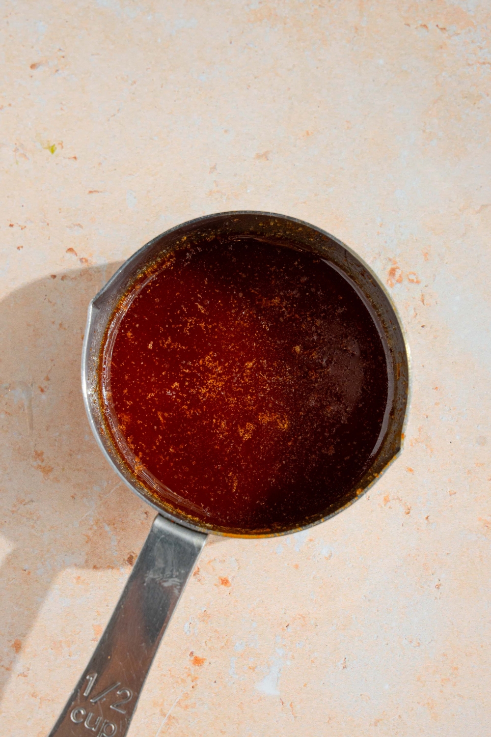 A small measuring cup with melted butter mixed with cajun spices. The cup is on a tan counter.