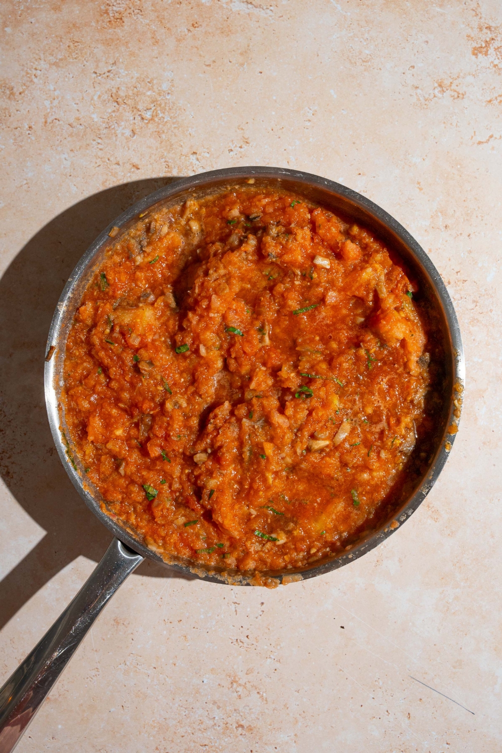A skillet with homemade spaghetti sauce with fresh tomatoes simmering. The skillet is on a tan counter.