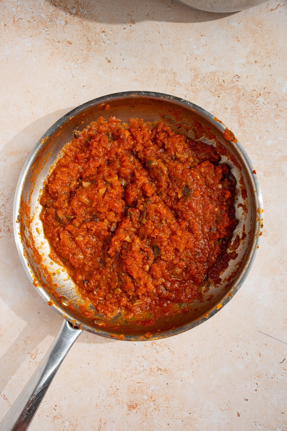 A skillet with cooked down homemade spaghetti sauce with fresh tomatoes. The skillet is on a tan counter.
