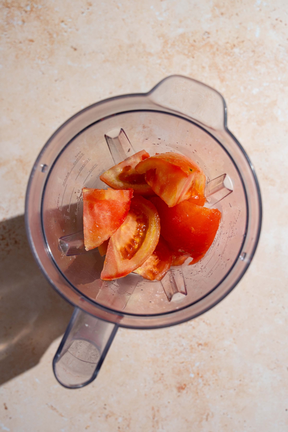 A blender with skinned and cubed tomatoes. The blender is on a tan counter.