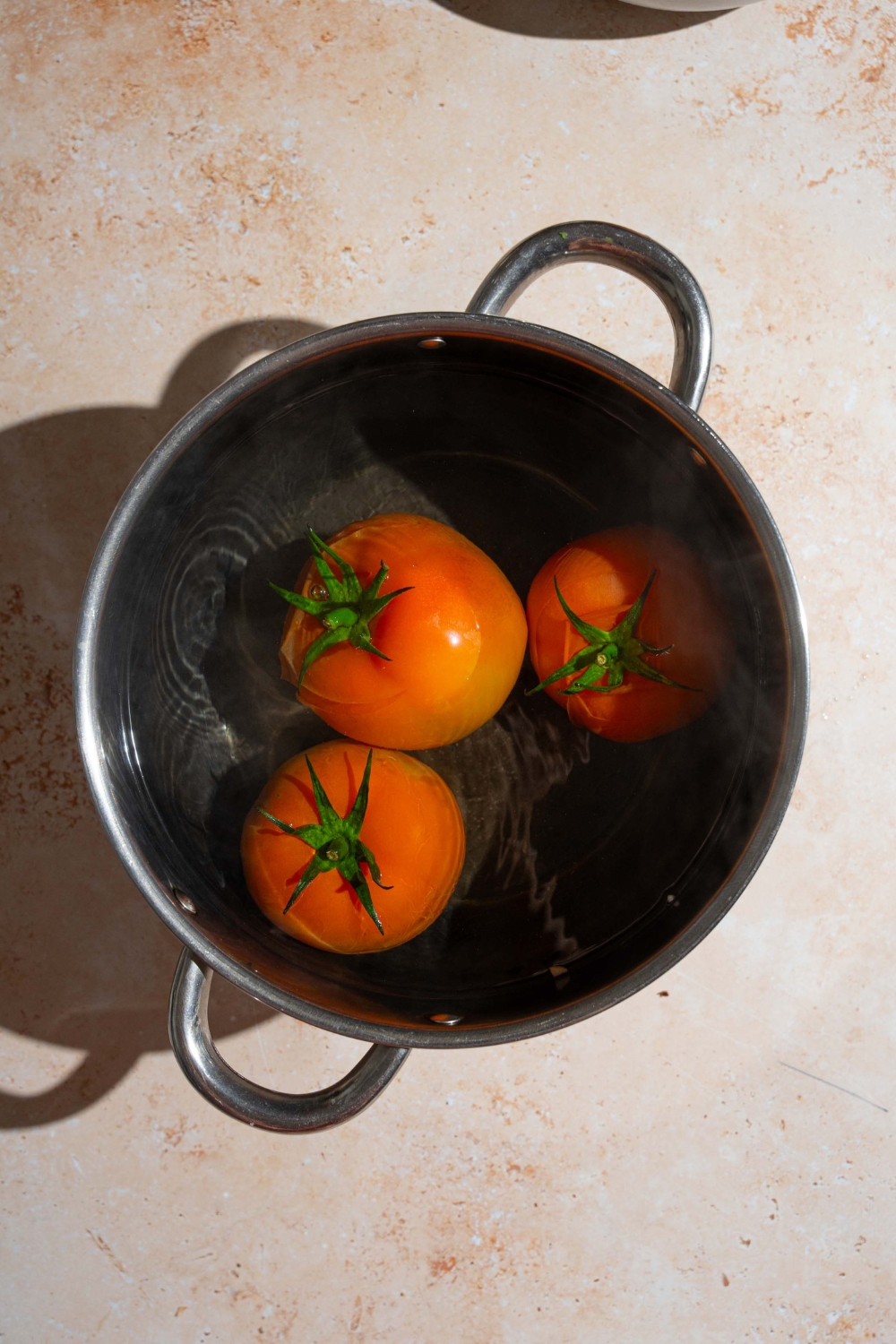 A stock pot with whole tomatoes blanching in water. The pot is on a tan counter.