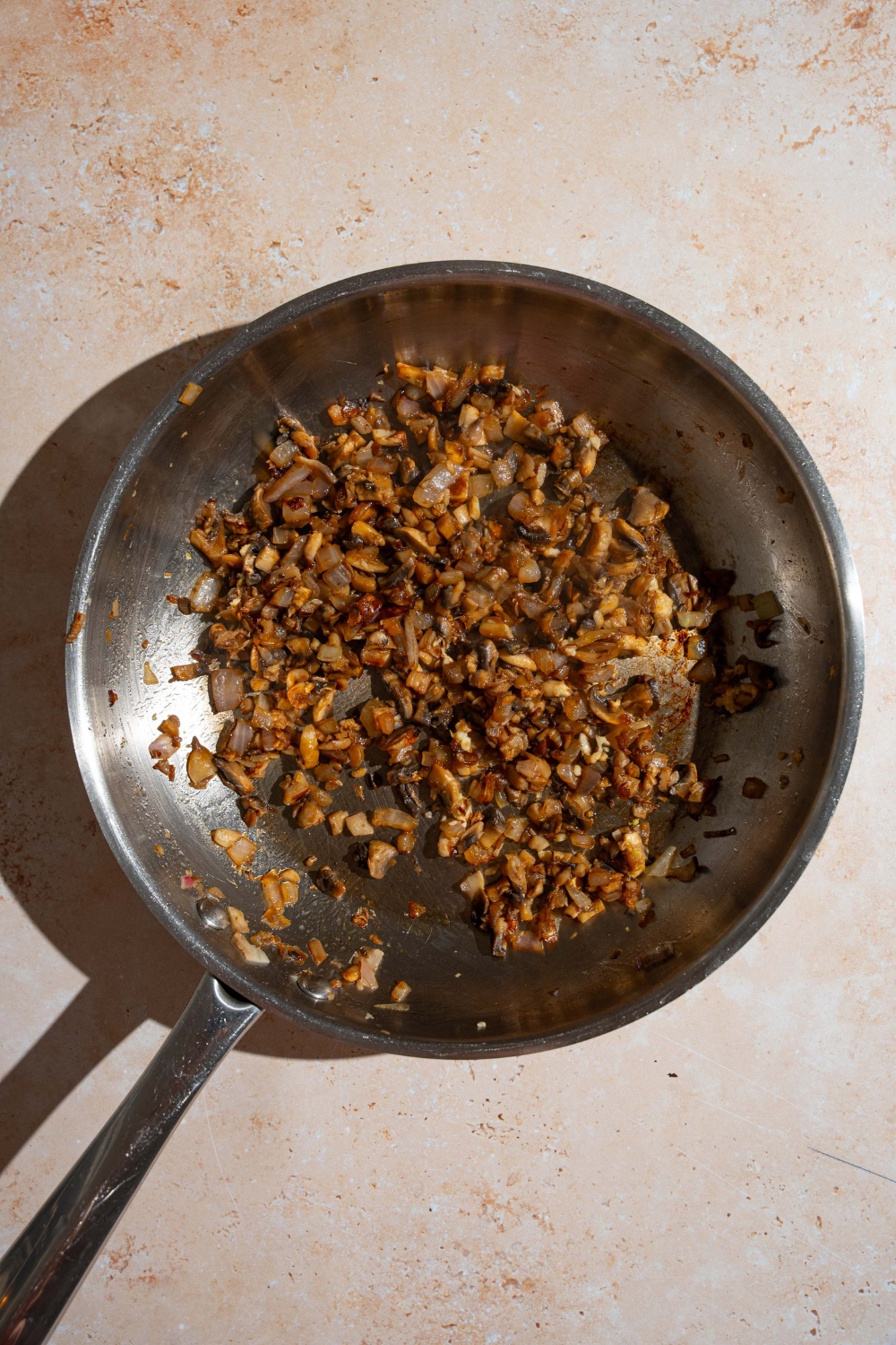 A skillet with sautéed diced mushrooms and onions tossed in soy sauce and garlic. The skillet is on a tan counter.