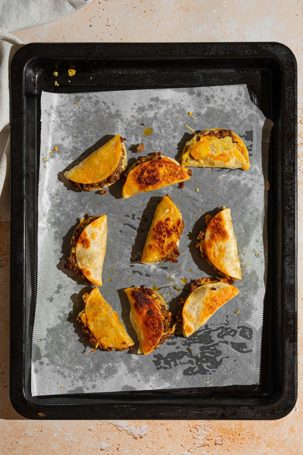 A baking sheet lined with parchment paper with baked mini beef tacos. The sheet is on a tan counter.