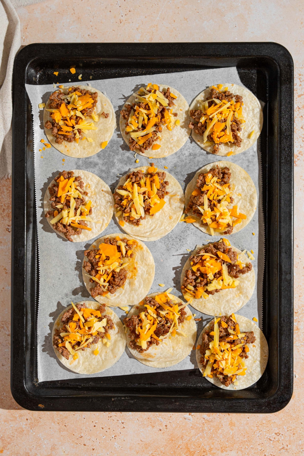 A baking sheet lined with parchment paper with open mini beef tacos. The sheet is on a tan counter.