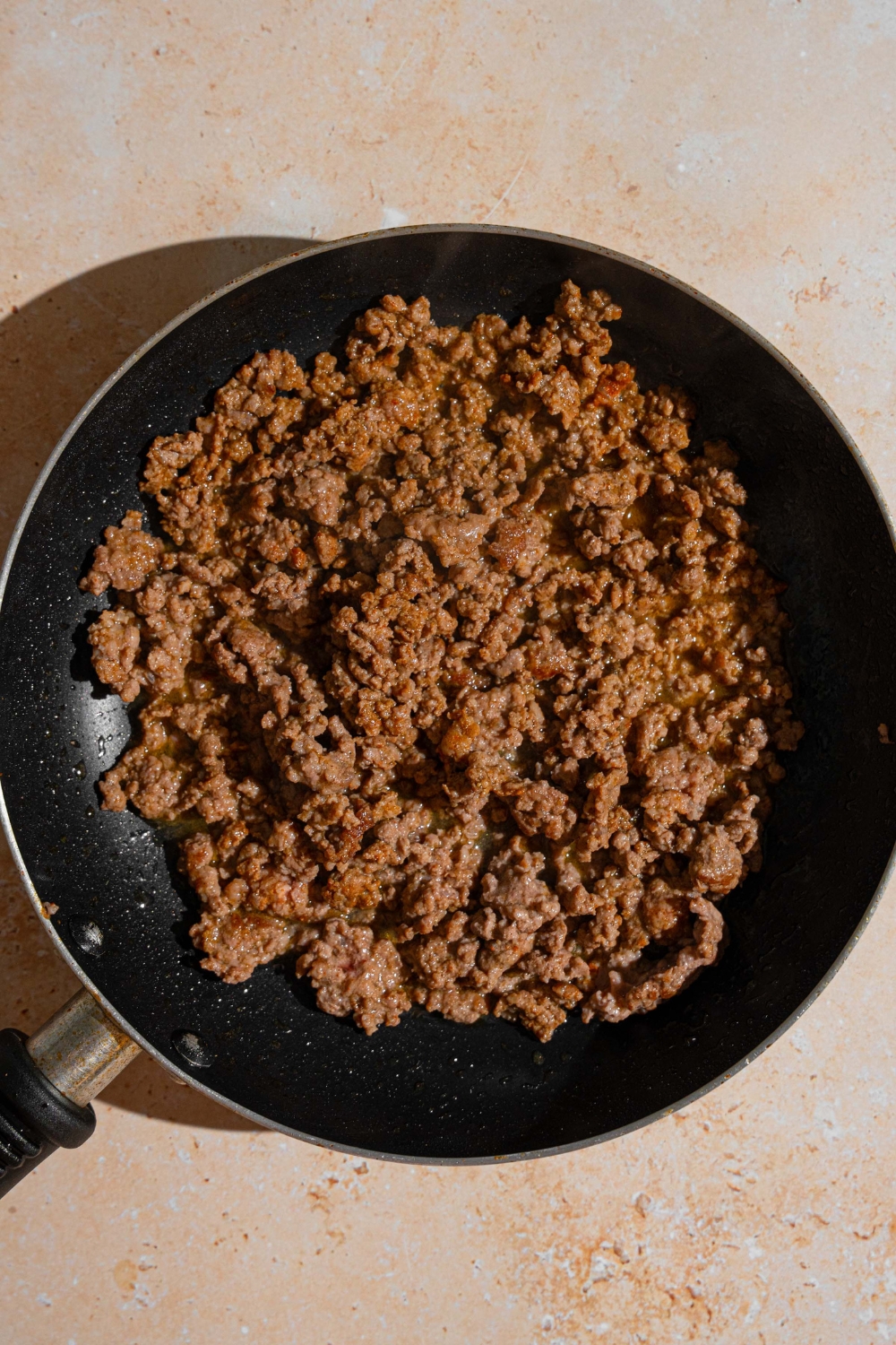 A skillet with cooked beef. The skillet is on a tan counter.