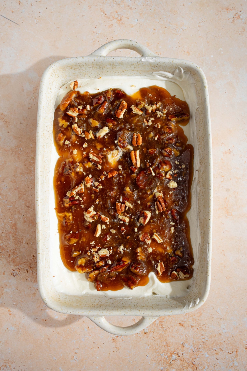 A white baking dish with an unchilled no bake cheesecake dip with pecan pie topping. The dish is on a tan counter.