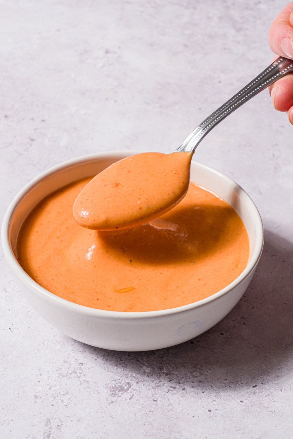 A small bowl with boom boom sauce with a spoon dipping into the sauce. The bowl is on a stone counter.