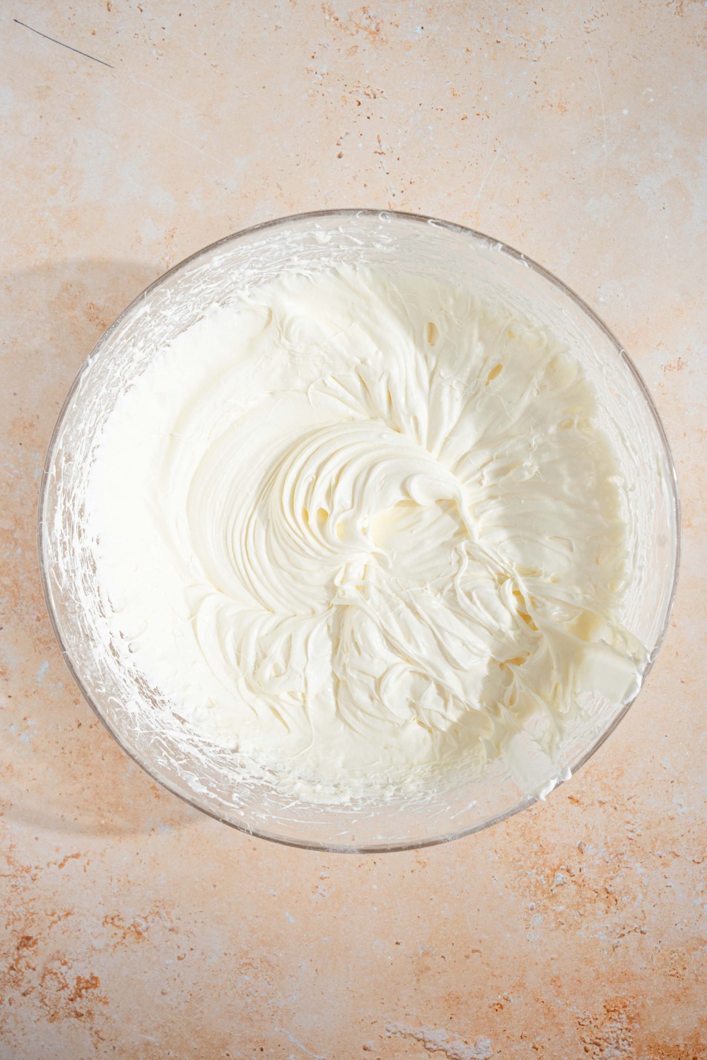 A large glass bowl with no bake cheesecake mixture including whipped cream, cream cheese, and powdered sugar. The bowl is on a tan counter.