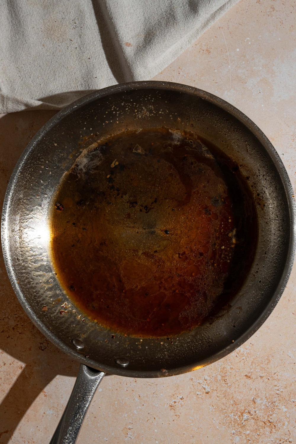 A skillet with reduced peppercorn sauce base. The skillet is on a tan counter.