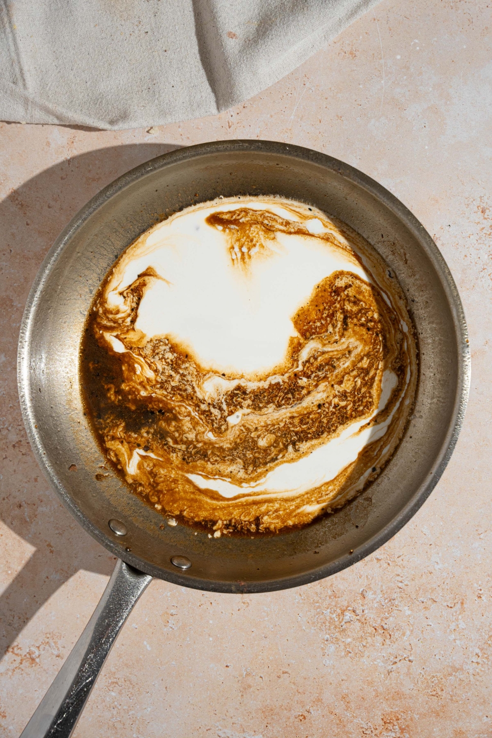 A skillet with peppercorn sauce base mixed with heavy cream. The skillet is on a tan counter.