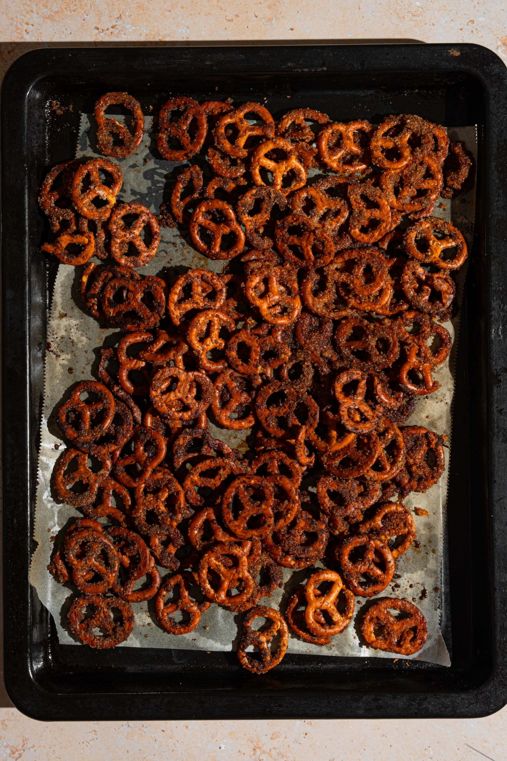 A baking sheet lined with parchment paper with baked cinnamon sugar pretzels. The sheet is on a tan counter.