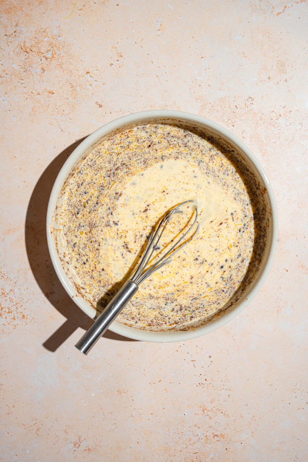 A bowl with a whisk mixing an egg and milk custard for bread pudding. The bowl is on a tan counter.