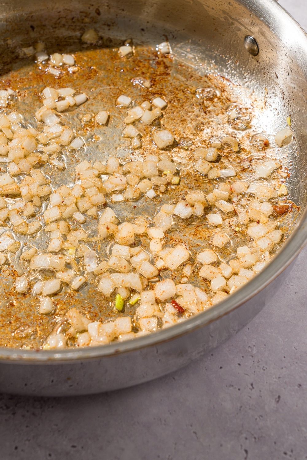 A skillet with diced onion sautéing in oil. The skillet is on a white counter.