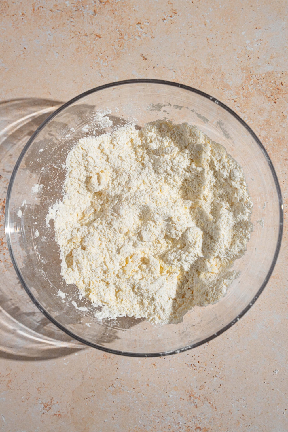 A glass bowl with cold butter shaped into a dry ingredients mixture for shortcake dough. The bowl is on a tan counter.