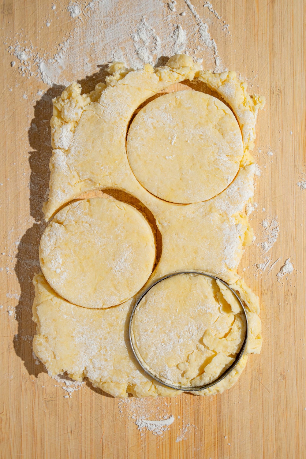 Rolled shortcake dough with flour on a wooden board. There are four shortcake cuts shaped into the dough.