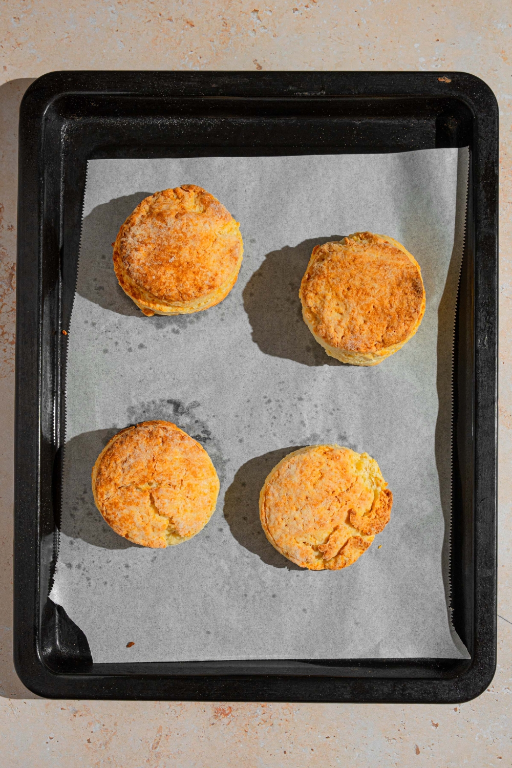 A baking sheet lined with parchment paper with four baked shortcake biscuits. The sheet is on a tan counter.