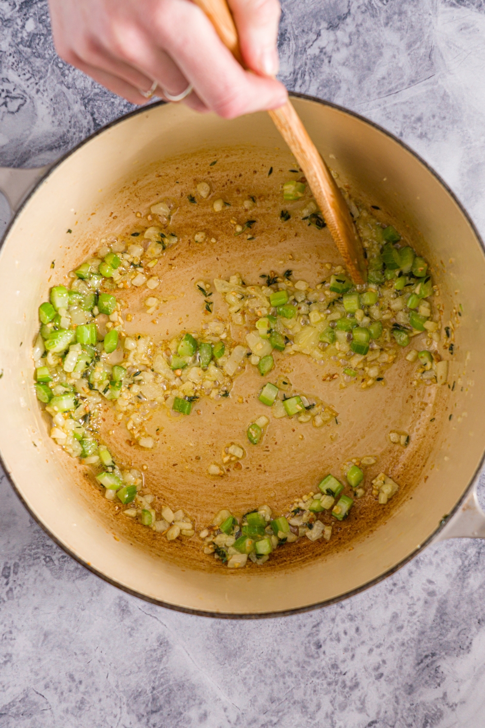 A dutch oven with chopped celery and onions sautéing in oil. The pot is on a marble counter.