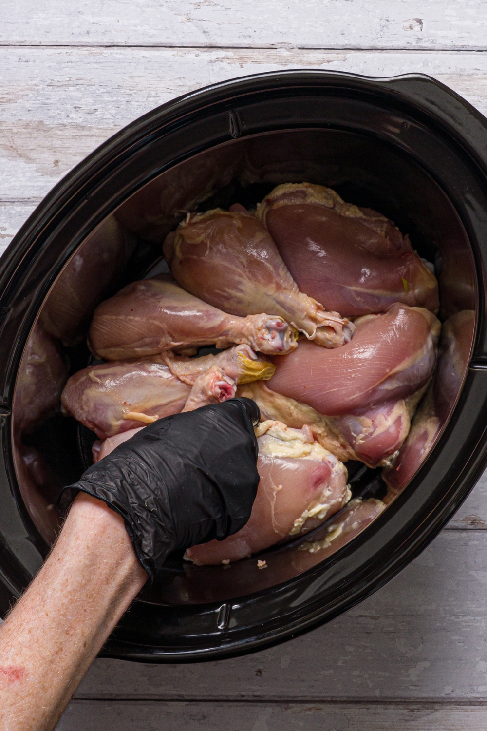A crockpot with a hand placing chicken into the slow cooker.