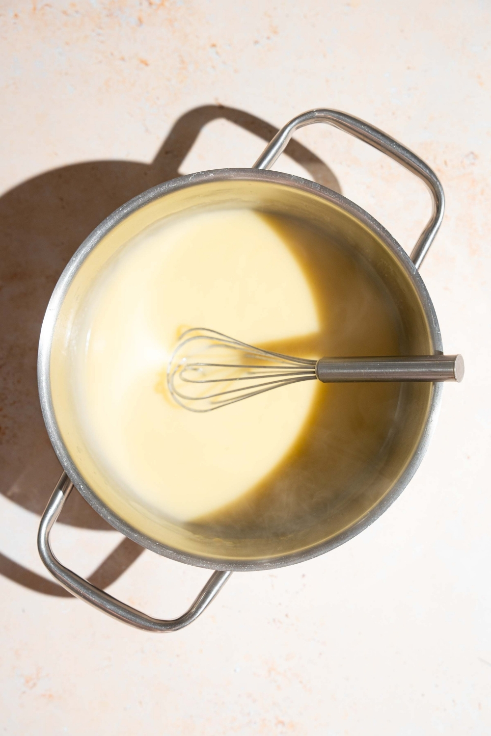 A stock pot with a whisk mixing a sour cream sauce base. The pot is on a tan counter.