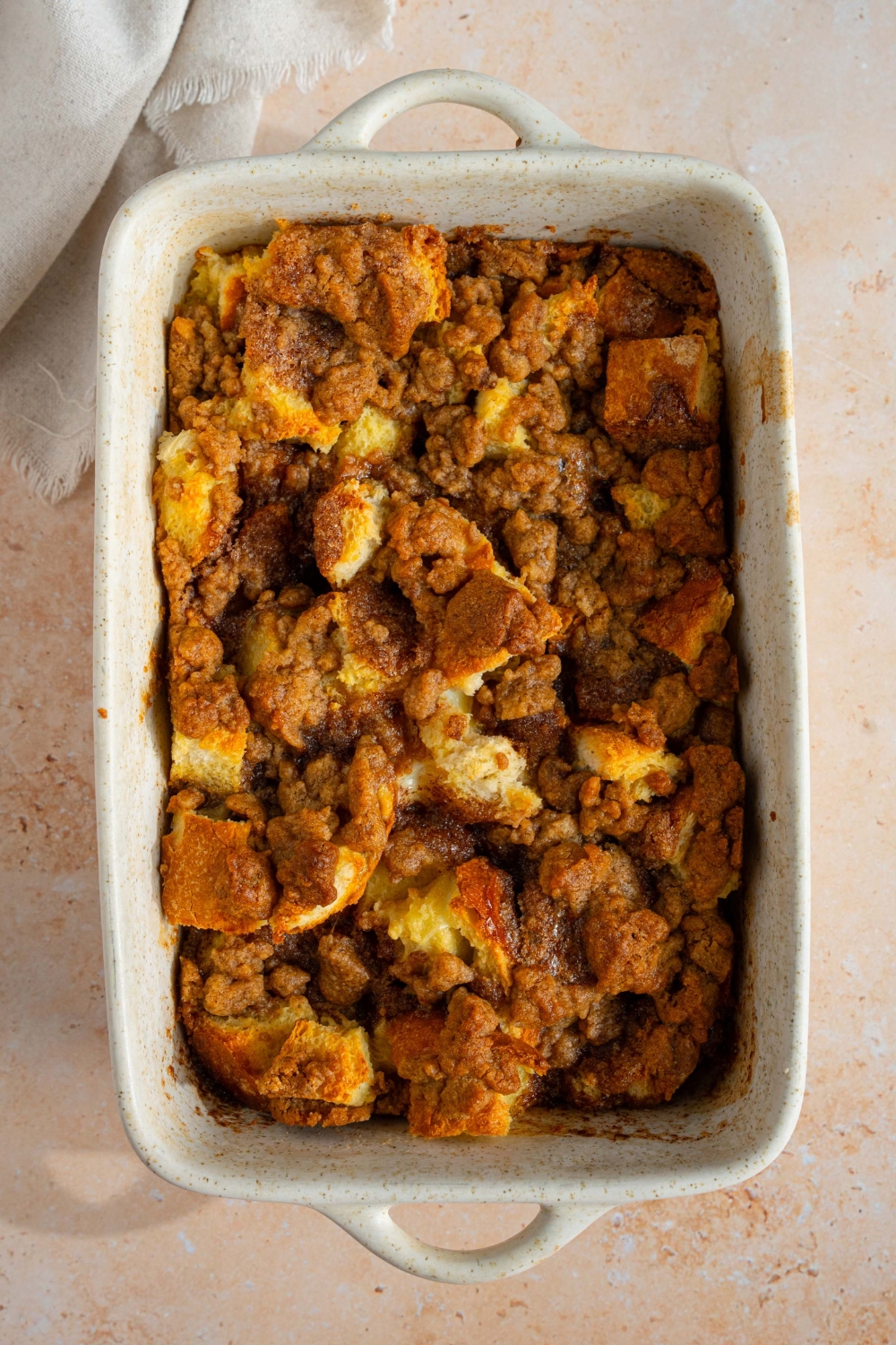 A ceramic baking dish with baked sourdough french toast casserole. The dish is on a tan counter with a white cloth napkin.