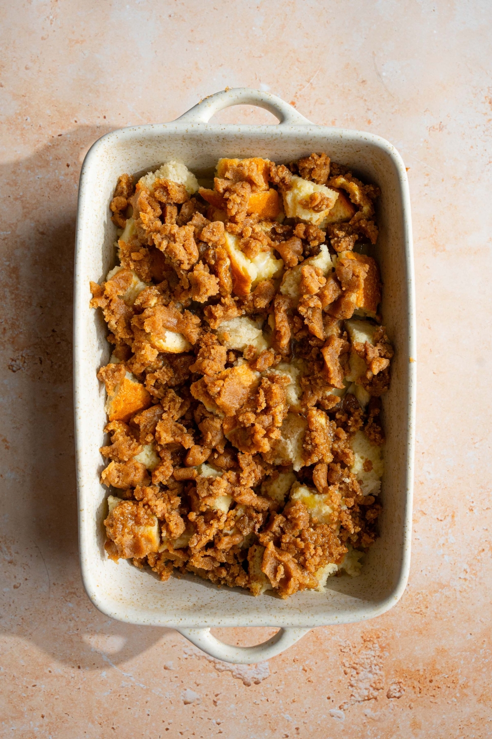 A ceramic baking dish with unbaked sourdough french toast casserole soaking in custard with a streusel topping. The dish is on a tan counter.